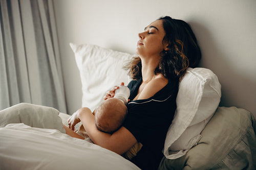 Tired mother bottle-feeding baby while resting in bed