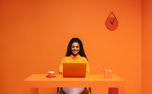 Young freelance woman working on laptop in vibrant orange monochromatic workspace