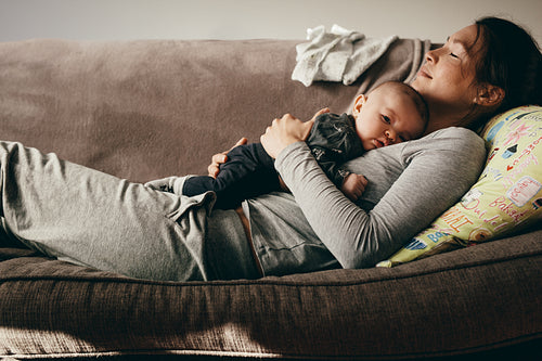 Mother sleeping on a couch with her baby on her