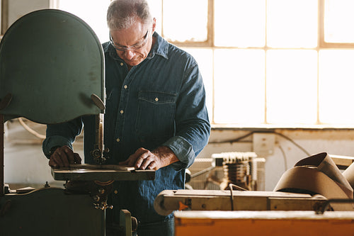 Carpenter in workshop cuts the wood using band saw
