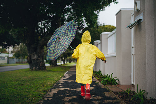 Girl in waterproof clothes and umbrella running outdoors