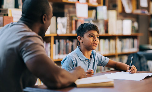 Young school boy having a lesson with his teacher in a library