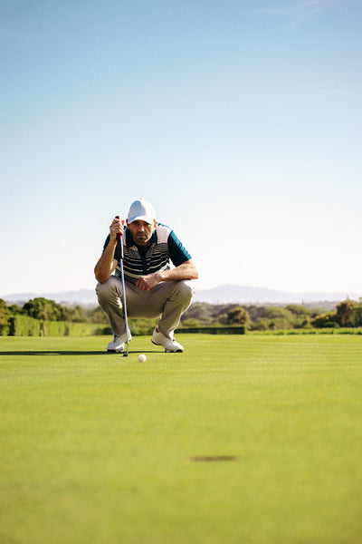 Man crouching on the green on a golf course aiming for the cup