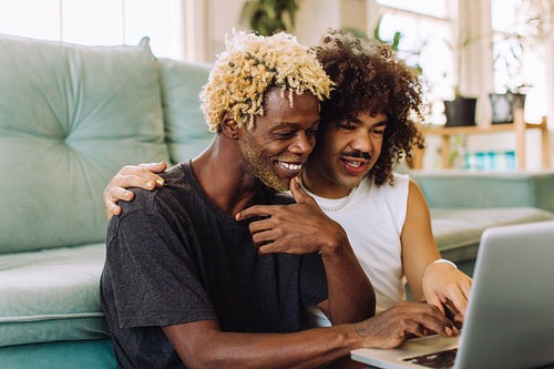 Cute gay couple using a laptop together at home