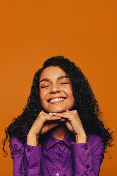 Vibrant smiling woman with curly hair on orange background