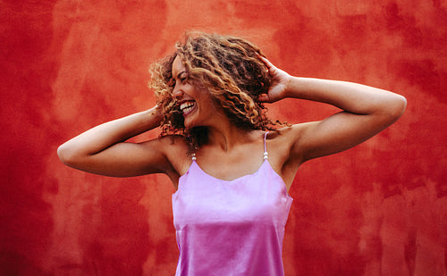 Happy woman shakes curly hair playfully against vibrant red wall