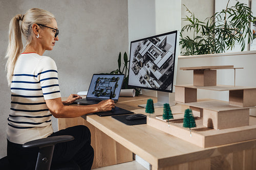 Architect working on building designs with computer and physical scale model