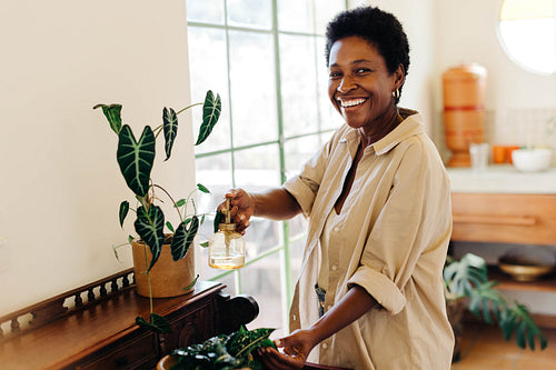 Happy Brazilian woman watering potted plants with spray bottle in a green indoor garden