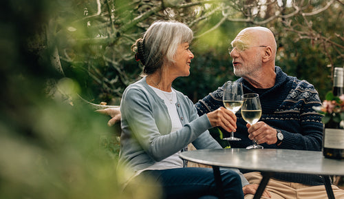 Senior couple toasting wine sitting in backyard