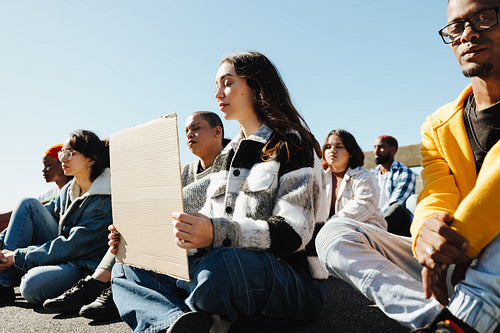 Group of protestors seated outdoors holding signs on a bright sunny day
