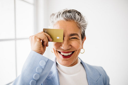 Mature female professional holding a gold credit card in an office