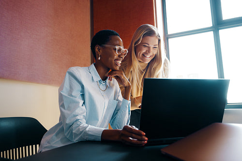 Two young women smiling while working together on a laptop