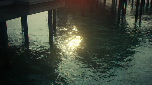 Golden sunlight reflections on calm tropical water under a serene pier in the morning