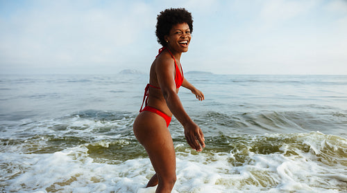 Joyful African woman enjoying the ocean waves at the beach