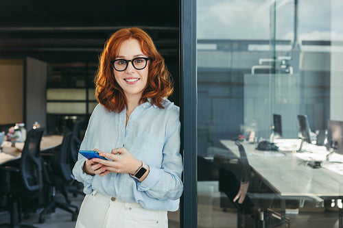 Young businesswoman using her smartphone in an office, happy employee in tech company