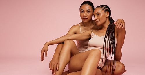 Two female models sitting over pink background