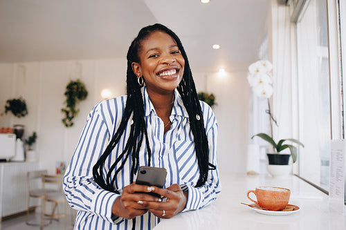 Portrait of a happy young businesswoman smiling at the camera while holding a smartphone in a cafe