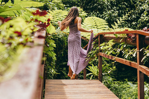 Woman in beautiful dress walking on wooden bridge in nature.