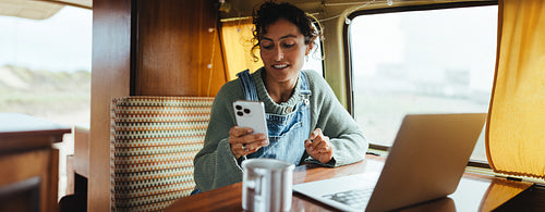 Working on the go: woman using phone and laptop in a cozy camper van interior