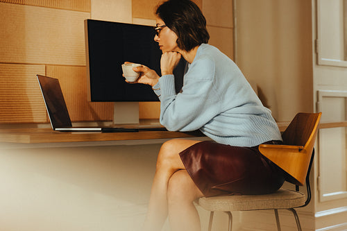 Woman works on a laptop at a desk with a coffee in office
