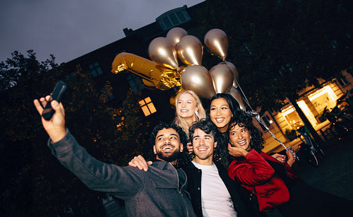 Group of friends celebrating with balloons and taking a selfie outdoors