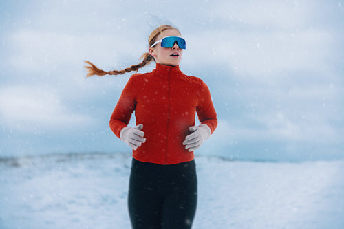Snowfall surrounds the running woman during winter fitness training outdoors
