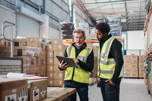Warehouse workers using a digital tablet while recording inventory