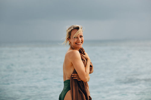 Smiling mature woman wrapped in a towel by the ocean