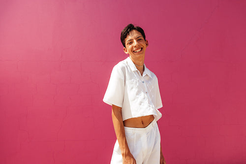 Happy teenage boy standing against a pink background