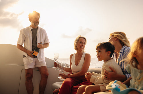 Family enjoying sunset cruise celebrating life with sparkling wine, while bonding and relaxing on a luxurious yacht