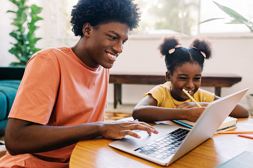 Teenage boy helping his sister with her homework, using a laptop for learning