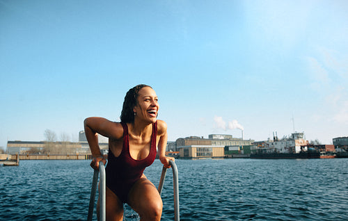 Happy woman climbing ladder after refreshing ocean swim on a winter day