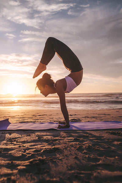 Woman in pincha mayurasana scorpion asana at beach
