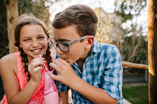 Happy young boy and girl drinking smoothie together