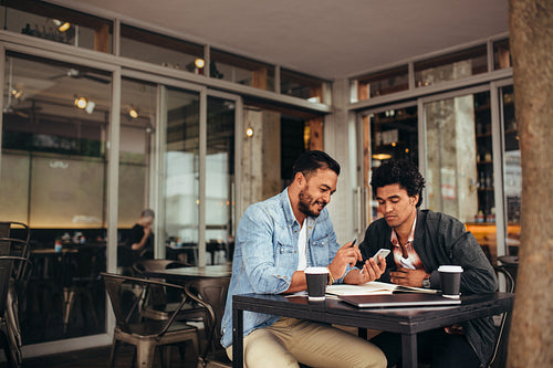 Two young men sitting at cafe using mobile phone