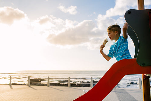 Boy eating an ice cream sitting on a slide