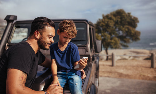 Father and son in front of car using smart phone