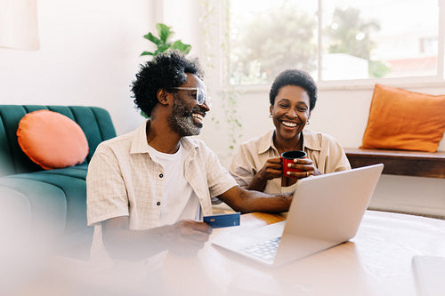 Happy black couple enjoying online shopping and electronic banking together in their living room