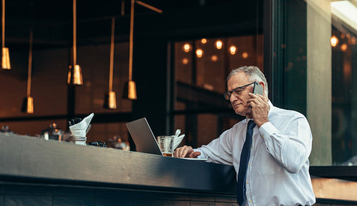 Senior businessman busy working from a cafe counter