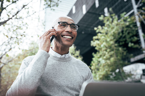 Businessman working on laptop computer and talking on mobile phone sitting outdoors