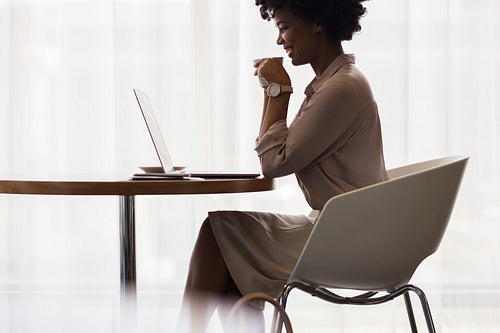 Office worker having coffee and looking at laptop
