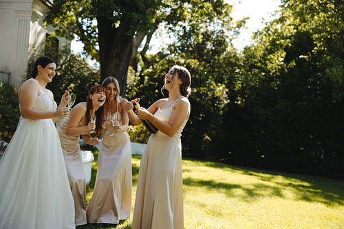 Bride celebrates with bridesmaids outdoors in sunlight surrounded by greenery