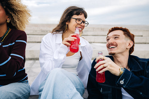 Candid friends laughing and sharing soda on steps