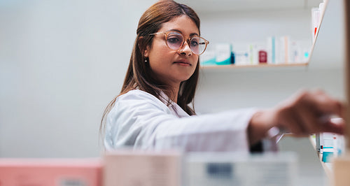 Female drug store worker getting prescription medication from a shelf