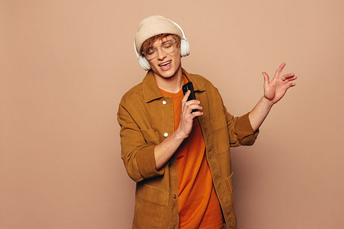 Cheerful man singing and dancing to music on smartphone in colorful studio