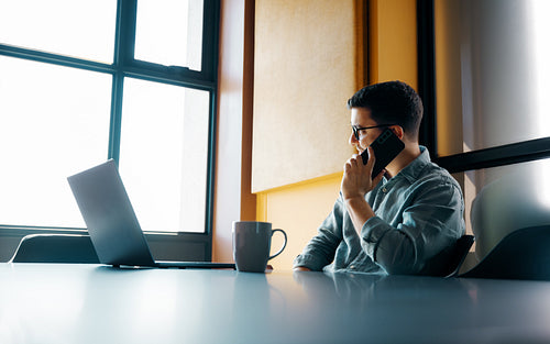 Young professional working in modern office using mobile phone and laptop