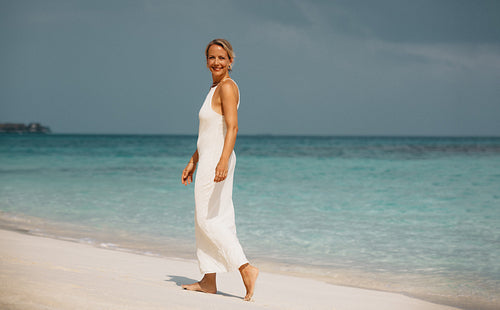 Woman in white dress walking along a serene tropical beach with clear waters