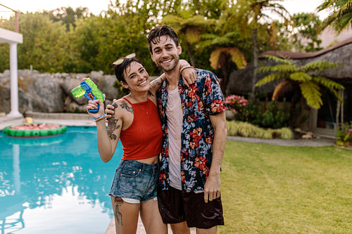 Cheerful couple by the pool with water gun