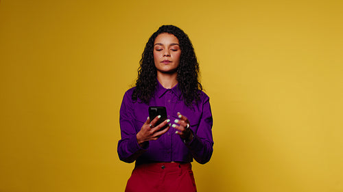 Young woman smiles while using phone on a colorful yellow background