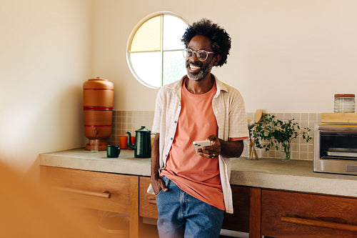 Afro man smiling in Brazilian kitchen, with a mobile phone in his hand